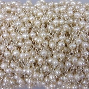 May include: A close-up of a white pearl and silver chain necklace. The chain is made of small, delicate links and the pearls are evenly spaced.