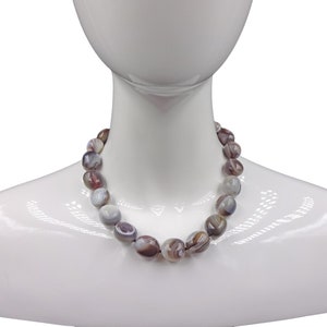 Puede incluir: Un collar hecho de cuentas de &aacute;gata marr&oacute;n y blanca. Las cuentas son de forma ovalada y tienen un acabado natural y pulido.
