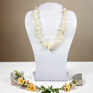 May include: A white iridescent shell necklace on a white mannequin bust. The necklace is made of irregular shaped pieces of shell.