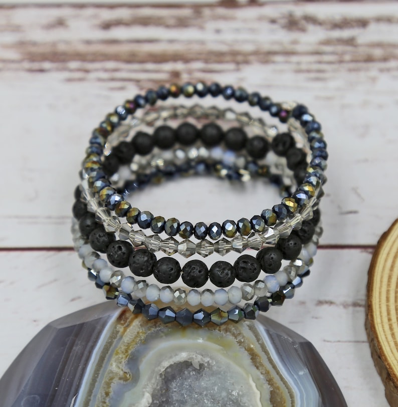 Puede incluir: Un brazalete de m&uacute;ltiples capas con cuentas de lava negra y cuentas de vidrio iridiscente. El brazalete est&aacute; apilado con m&uacute;ltiples hileras de cuentas, creando un aspecto en capas y texturizado.