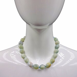 Puede incluir: Un collar de piedras preciosas azul claro y verde con cuentas de forma ovalada. El collar est&aacute; en un maniqu&iacute; blanco.