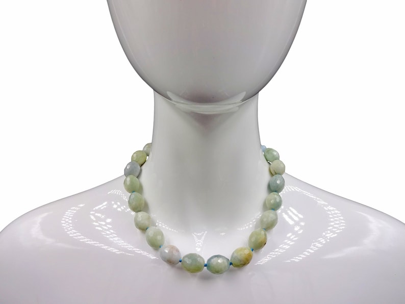 Puede incluir: Un collar de piedras preciosas azul claro y verde con cuentas de forma ovalada. El collar est&aacute; en un maniqu&iacute; blanco.