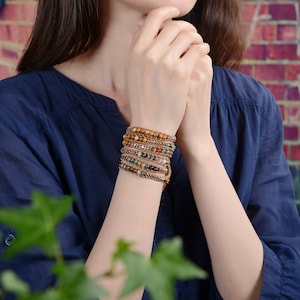 Op de afbeelding: Een meerlaags armband met bruin lederen koord, agaat kralen en goudkleurige metalen accenten.
