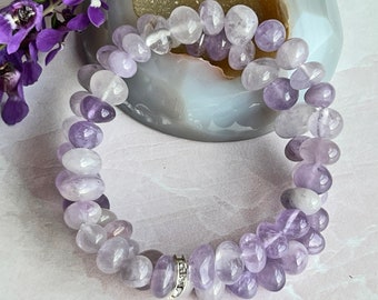 May include: A purple amethyst gemstone bracelet with a silver charm. The bracelet is made of smooth, rounded beads.
