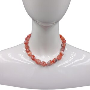 Puede incluir: Un collar hecho de cuentas de cornalina. Las cuentas son de color naranja intenso con vetas blancas y son ligeramente irregulares.