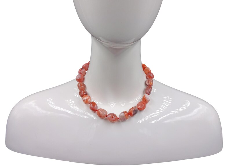 Puede incluir: Un collar hecho de cuentas de cornalina. Las cuentas son de color naranja intenso con vetas blancas y son ligeramente irregulares.