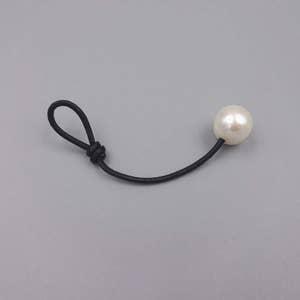 Puede incluir: Un collar sencillo de cordón negro con un solo colgante de perla blanca.