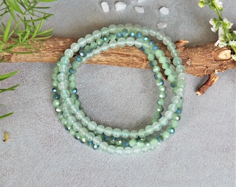 May include: A layered bracelet made of green and blue glass beads. The beads are round and have a frosted finish. The bracelet is on a wooden surface.
