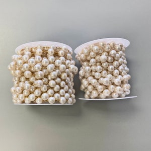 May include: Two spools of white pearl and gold chain, each wrapped in white paper.