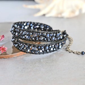 May include: A black beaded bracelet with a silver chain accent. The bracelet is made of small, faceted beads that are wrapped in wire.