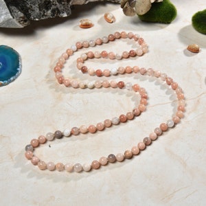 May include: A long strand of pink, white and brown gemstone beads strung on a gold thread. The beads are round and have a natural, polished finish.