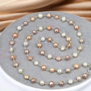 May include: A long silver chain necklace with small, round, pastel-colored pearls. The pearls are in shades of white, pink, and peach.