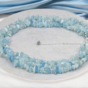 May include: A light blue aquamarine chip necklace with a silver chain and clasp. The necklace is made of many small, irregular shaped chips of aquamarine.