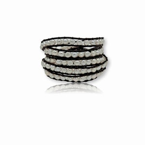 May include: A multi-wrap bracelet made of brown leather and white pearls. The bracelet is wrapped around itself several times, creating a layered effect.