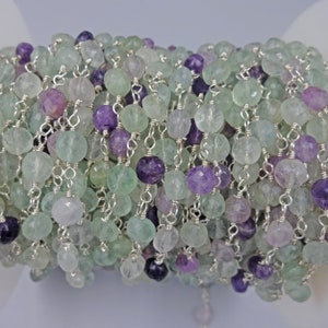 May include: A strand of green and purple gemstone beads strung on a silver chain. The beads are faceted and have a natural, irregular shape.