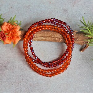 May include: A multi-strand bracelet made of small, round, orange and red beads. The beads are arranged in a circular pattern and are strung on a clear elastic cord.