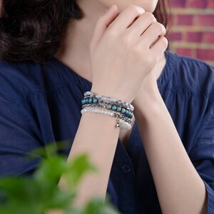 Puede incluir: Un conjunto de cinco pulseras con cuentas azules y blancas. Las pulseras est&aacute;n apiladas en la mu&ntilde;eca de una persona.
