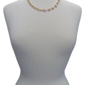 May include: A gold chain necklace with a row of white pearls on one side. The necklace is displayed on a white mannequin.