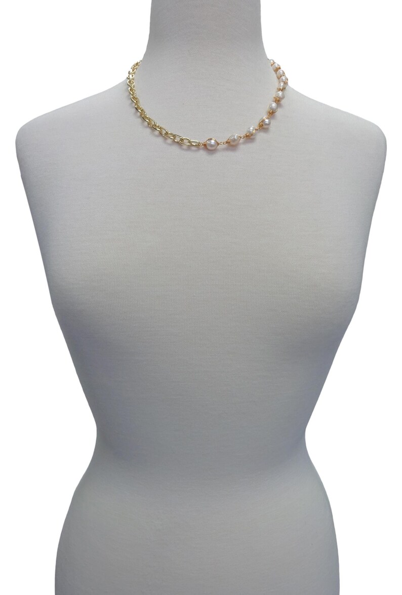 May include: A gold chain necklace with a row of white pearls on one side. The necklace is displayed on a white mannequin.