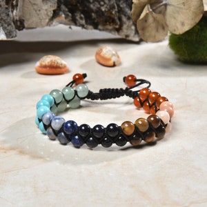 May include: A multi-colored beaded bracelet with a black cord. The beads are arranged in a rainbow pattern, starting with green, turquoise, blue, dark blue, brown, and ending with pink.