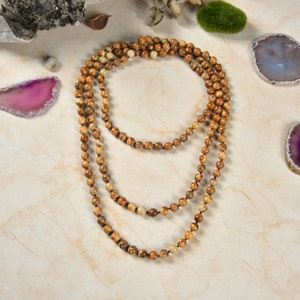May include: A long, layered necklace made of brown and beige gemstone beads. The necklace is made of multiple strands of beads, and the beads are all different sizes and shapes.