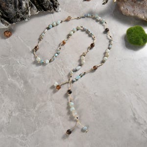 May include: A long, layered necklace featuring blue, brown and white beads. The necklace is crafted from natural stones and has a simple, elegant design.