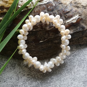 Puede incluir: Un brazalete de perlas blancas hecho de perlas de forma irregular. El brazalete está sobre una superficie de madera.