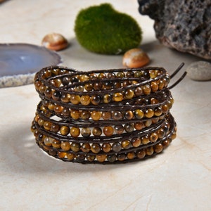 May include: A multi-strand bracelet made with brown leather cord and tiger's eye beads. The bracelet is wrapped around itself to create a layered look.