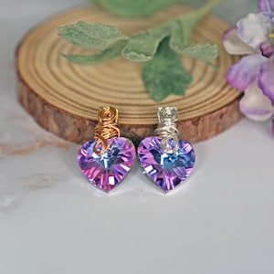 May include: Two heart-shaped crystal pendants with iridescent purple and blue hues. Each pendant is wrapped with wire, one in gold and one in silver.