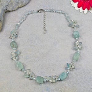 Könnte beinhalten: Zarte Aquamarin-Halskette mit unregelmäßigen, hellblau-grünen Edelsteinen, durchsetzt mit kleinen, klaren Perlen und Clustern aus weißen Akzenten. Die Halskette hat einen silberfarbenen Verschluss und eine Verlängerungskette.