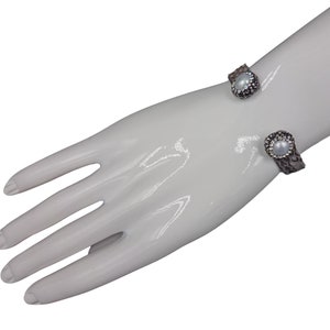 May include: A silver cuff bracelet with a faux snakeskin design and two pearl accents.