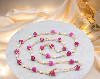 May include: A long pink and white beaded necklace with a delicate chain and small pink beads. The necklace is made of natural materials and has a simple, elegant design.