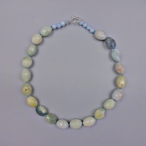 Puede incluir: Un collar de piedras preciosas de aguamarina azul claro con un cierre de plata. El collar est&aacute; hecho de cuentas ovaladas con un acabado facetado.