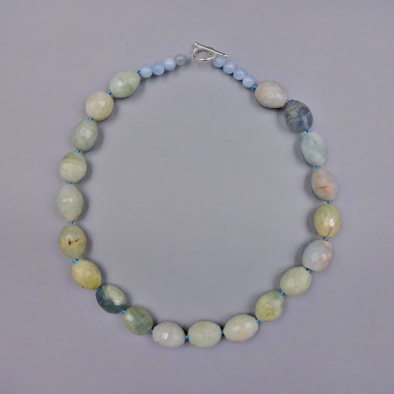 Puede incluir: Un collar de piedras preciosas de aguamarina azul claro con un cierre de plata. El collar est&aacute; hecho de cuentas ovaladas con un acabado facetado.