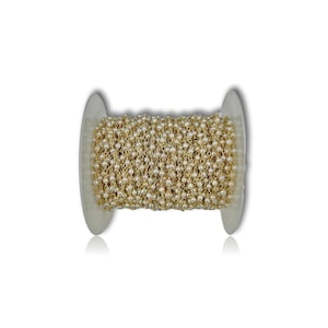 May include: A spool of gold chain with white pearl beads. The chain is wound around the spool and is ready to be used for jewelry making.