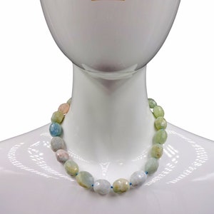 Puede incluir: Un collar hecho de cuentas de piedras preciosas de color azul claro, verde y rosa. Las cuentas son de forma ovalada y tienen un acabado facetado.