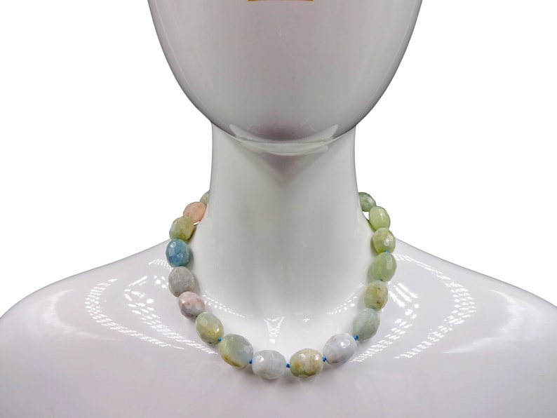 Puede incluir: Un collar hecho de cuentas de piedras preciosas de color azul claro, verde y rosa. Las cuentas son de forma ovalada y tienen un acabado facetado.