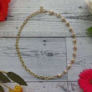 May include: A gold chain necklace with a pearl and gold chain design. The necklace is on a white wooden background.