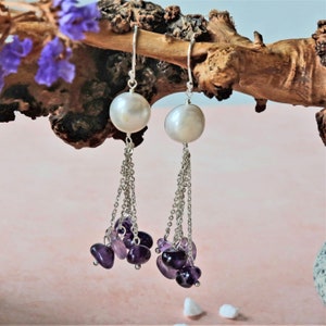 May include: Silver dangle earrings with a white pearl and a cluster of purple amethyst stones.