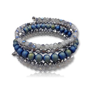 Puede incluir: Un brazalete de m&uacute;ltiples hilos con cuentas azules, verdes y plateadas. El brazalete est&aacute; hecho de varios hilos de cuentas que se envuelven entre s&iacute;.