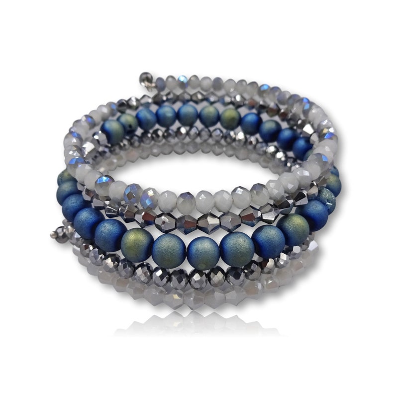Puede incluir: Un brazalete de m&uacute;ltiples hilos con cuentas azules, verdes y plateadas. El brazalete est&aacute; hecho de varios hilos de cuentas que se envuelven entre s&iacute;.