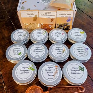 May include: A collection of organic herbal tea products, including tins of various tea blends and packets of loose herbs. The image features a tea infuser and a box with the text "Make Your Own Cup Of Herbal Tea Kit."