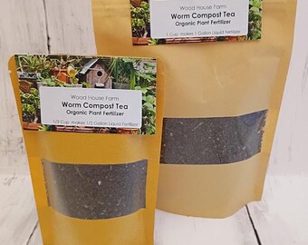 May include: Two tan stand-up pouches containing dark organic worm compost tea plant fertilizer. Each label features a garden image and text: Wood House Farm, Worm Compost Tea, Organic Plant Fertilizer, and mixing instructions.