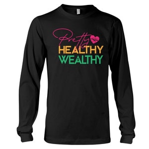 Może przedstawiać: Czarny T-shirt z długim rękawem z napisem "Pretty Healthy Wealthy" w kolorze różowym, pomarańczowym i zielonym. Różowe serce z czerwonym nadrukiem ust znajduje się nad tekstem.