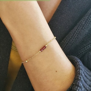 Könnte beinhalten: Ein goldenes Kettenarmband mit kleinen roten Perlen. Das Armband wird am Handgelenk einer Person gezeigt. WRIST: 5.75" IN BRACELET: MEDIUM (6.5" to 6.75" in)