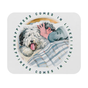 Puede incluir: Un posavasos cuadrado con una ilustración en acuarela de una persona acariciando a un perro blanco y esponjoso. El perro tiene la lengua fuera. El texto "Happiness Comes in Licks" está impreso en verde alrededor del borde.