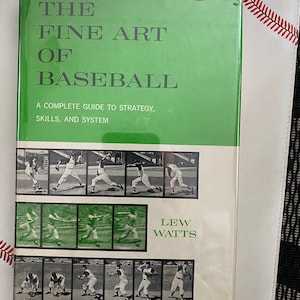 May include: A green book titled "The Fine Art of Baseball" by Lew Watts. The book cover features a complete guide to strategy, skills, and system. The cover also includes black and white photos of baseball players in action.