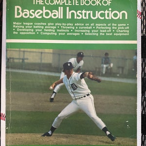 May include: A white book with a green cover and the title "The Complete Book of Baseball Instruction" in black text. The cover features a baseball player in a white uniform throwing a ball. The book is by Dell Bethel.