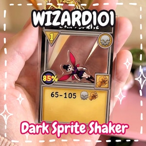 Peut inclure: Un porte-clés shaker en acrylique transparent représentant une carte de jeu Wizard101 Dark Sprite. La carte présente une illustration centrale d'un sprite sombre aux ailes rouges, une case jaune avec le texte 65-105, une icône de précision 85% et des symboles de crâne et de poing.