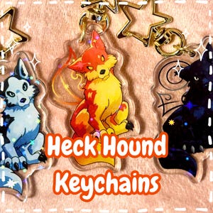 May include: Three Heck Hound keychains with star-shaped clasps. The keychains feature cartoon-style illustrations of dogs in various colors: white and blue, orange and yellow, and black. The text "Heck Hound Keychains" is displayed.